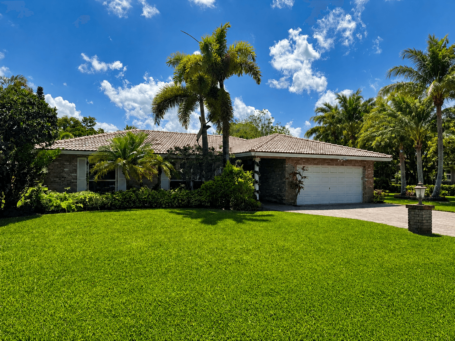 Brick house with a tiled roof, white garage, and palm trees on a sunny day.